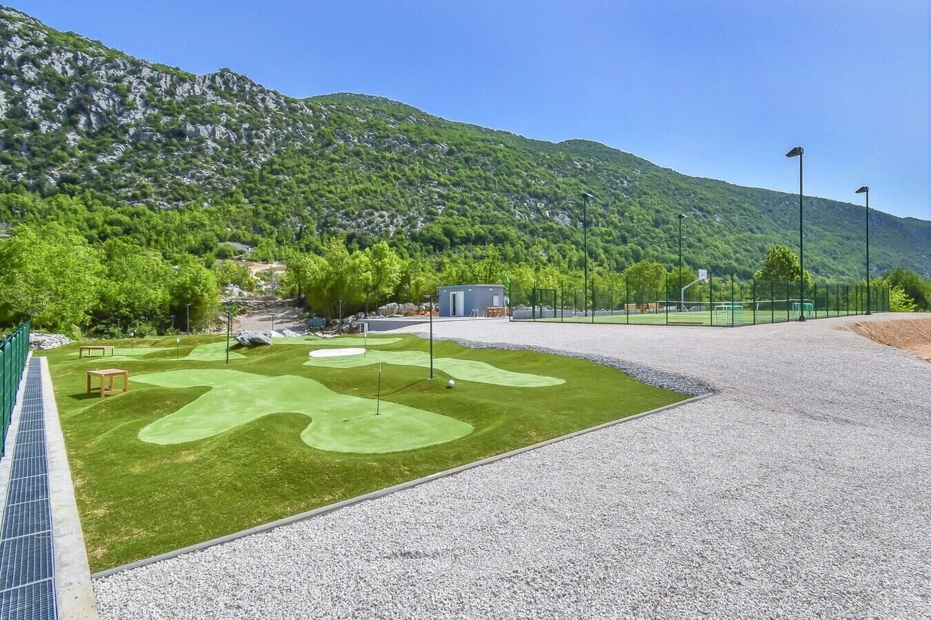A golf course with a well-maintained green, a gravel path, and a mountain backdrop.