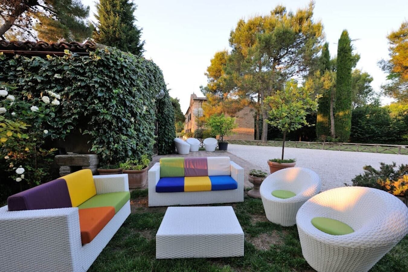 An outdoor seating area with wicker furniture and cushions, surrounded by greenery and trees.