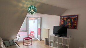 Una sala de estar moderna con un sofá, un televisor sobre un mueble blanco, un sillón rojo y un cuadro colorido en la pared.