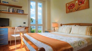 Un dormitorio con cama, escritorio, silla, televisor y un cuadro en la pared.