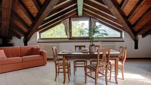 Un comedor con una mesa y sillas de madera, un sofá rojo estampado y un ventanal con vistas a árboles.