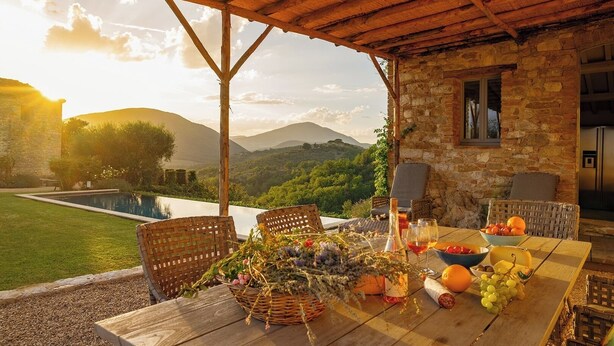 Ein rustikales Steinhaus mit Holztisch, gedeckt für eine Mahlzeit, mit Blick auf eine üppige Landschaft und einen Pool.