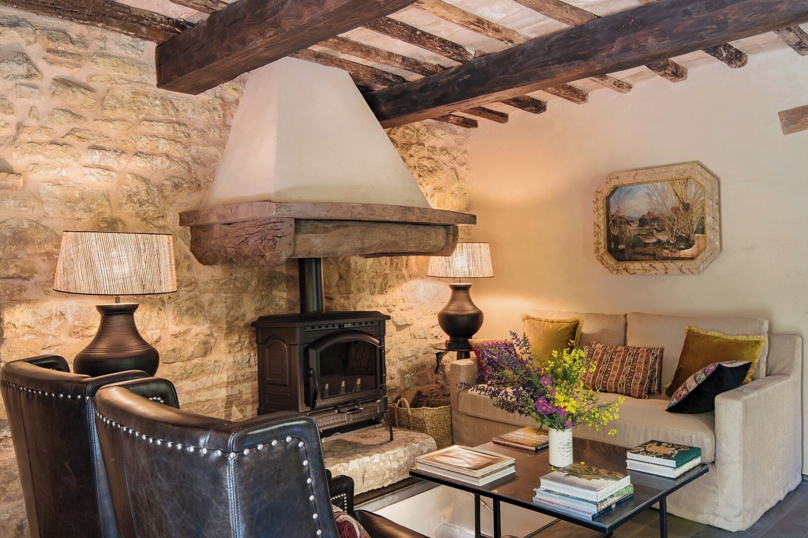 Una sala de estar acogedora con una pared de piedra, una chimenea, sillones de cuero, un sofá y un cuadro en la pared.