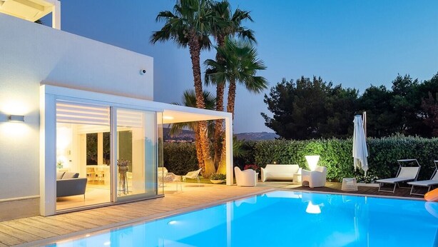 Un espace piscine extérieur moderne doté d’un patio fermé par des baies vitrées, de chaises longues et offrant une vue sur le paysage environnant.