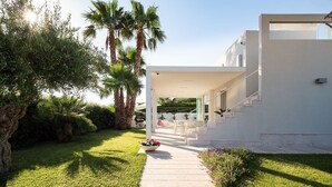 Une maison moderne dotée d’un espace extérieur aménagé avec un coin salon couvert, d’une pelouse bien entretenue et d’un chemin menant à l’entrée.