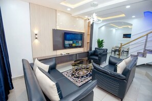 A modern living room with a flat-screen TV, leather sofas, a coffee table, and a staircase. - Iris-gold apartments (Ibadan)