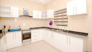 A modern kitchen with white cabinets, a stainless steel oven, and a built-in microwave. - Iris-gold apartments (Ibadan)