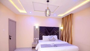 A modern bedroom with a large bed, a headboard, a bedside table, and a hanging light fixture. - Iris-gold apartments (Ibadan)