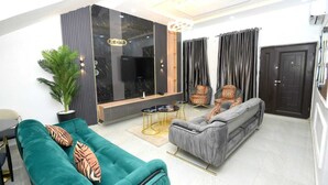 A modern living room with a teal sofa, a grey sofa, and a black accent wall. - Iris-gold apartments (Ibadan)