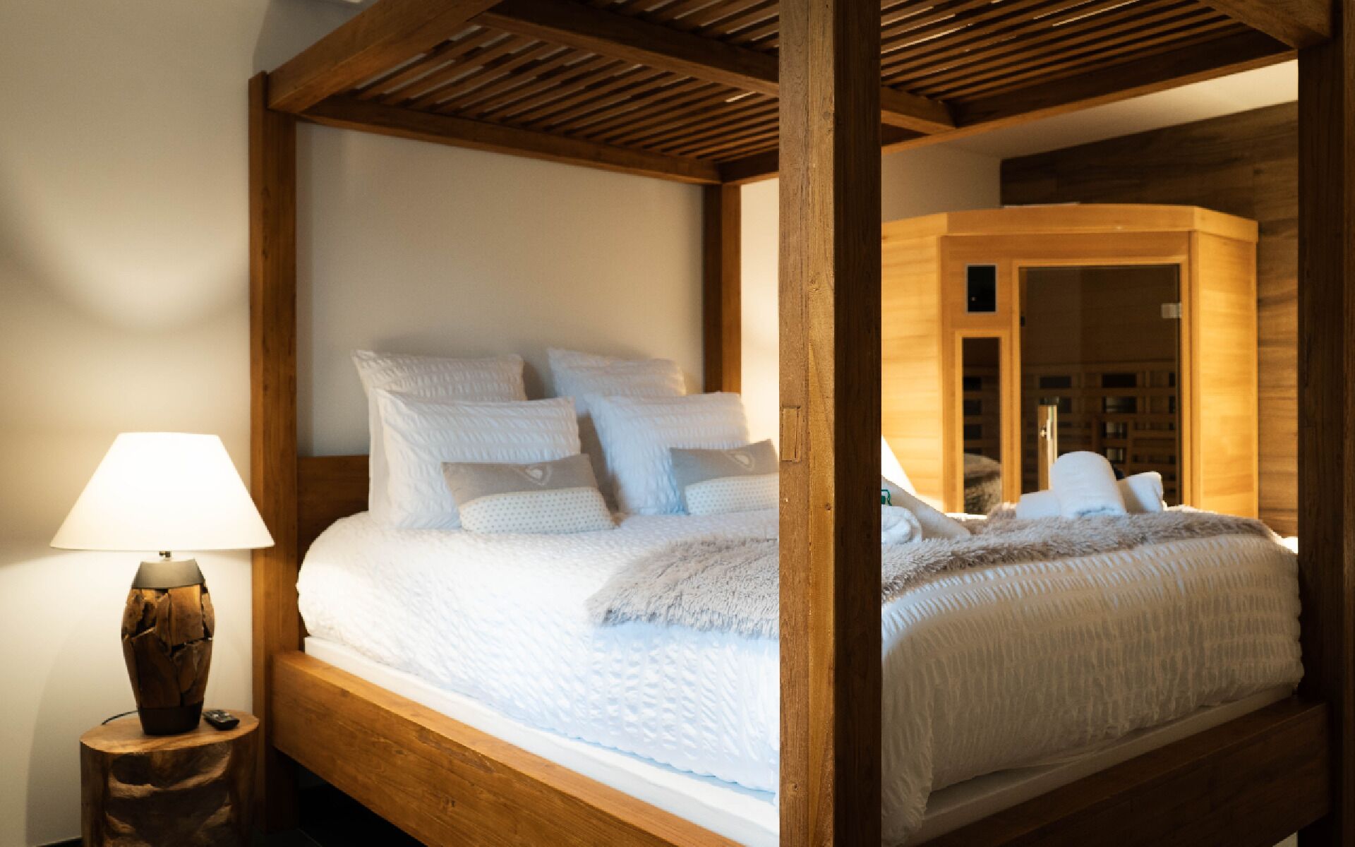 Un lit à baldaquin en bois, avec une literie blanche, une lampe de chevet et une table de chevet en bois.