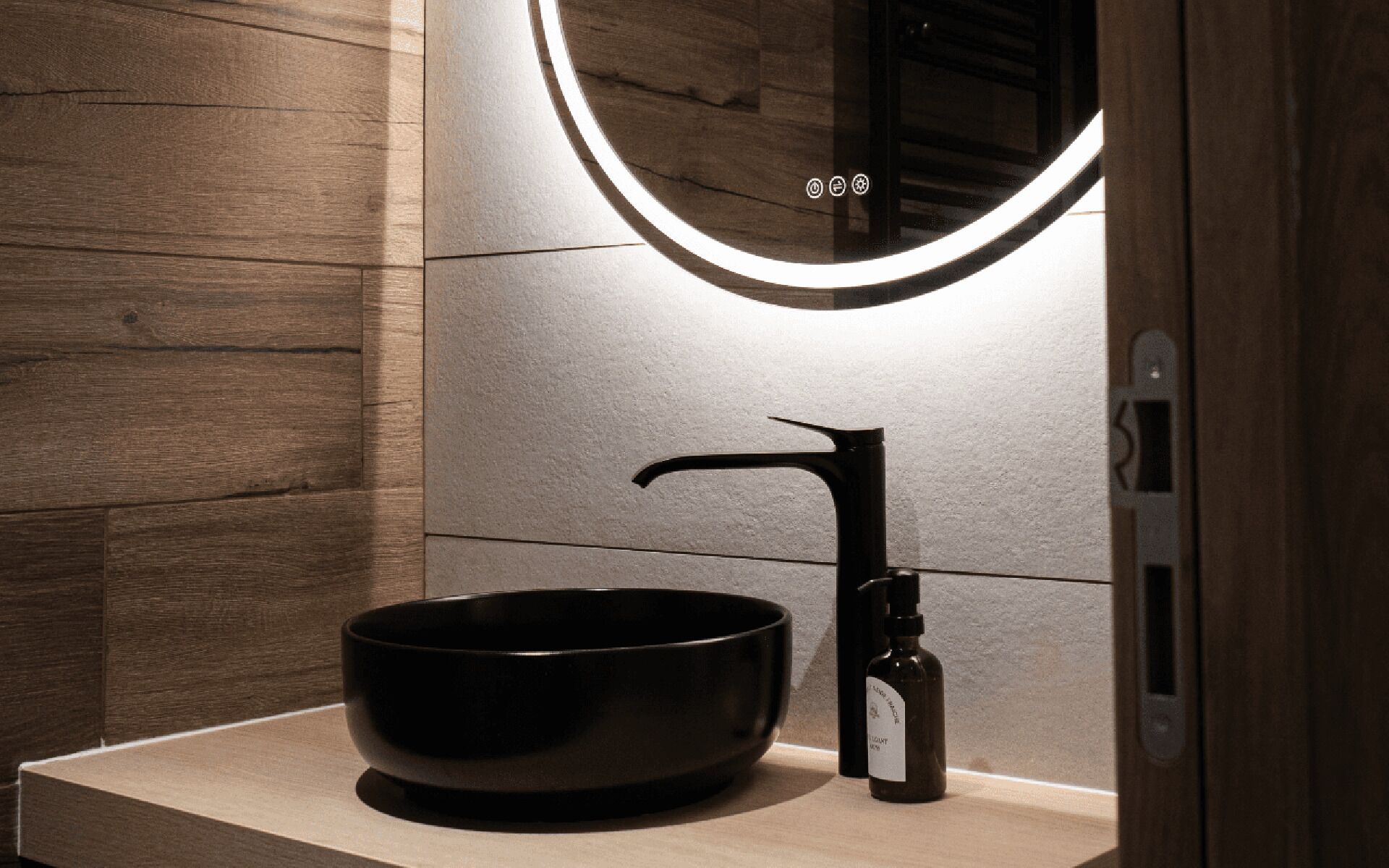 Une salle de bain moderne avec un mur en bois, un lavabo noir et un miroir avec éclairage intégré.
