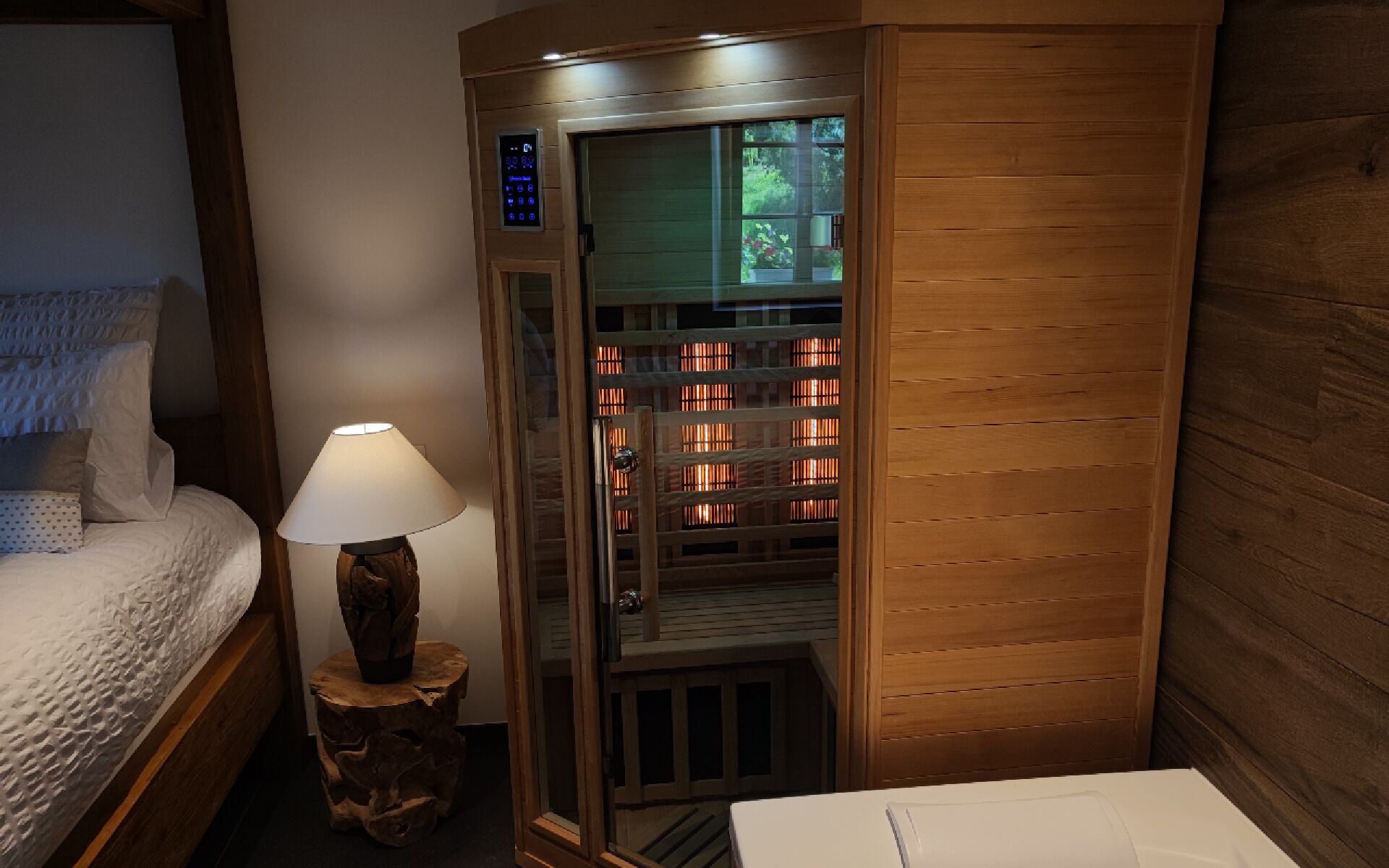 Ett hotellrum med en säng, ett träskåp med en glasdörr och en lampa på en träpall.