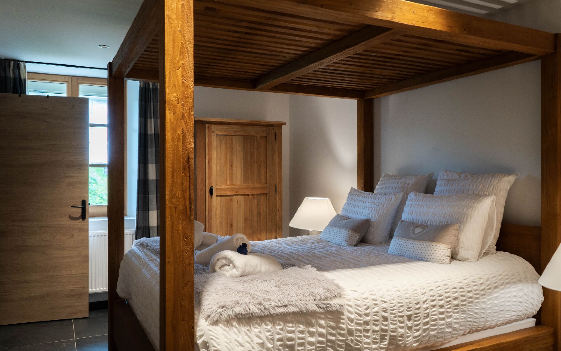 Ein Schlafzimmer mit einem Himmelbett, einem Holzschrank und einem Fenster mit Vorhängen.
