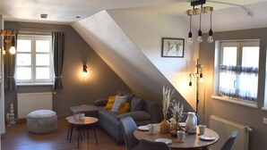 Un espacio habitable estilo loft acogedor, con comedor, un sofá con cojines, un taburete redondo y una mesa lista para comer.