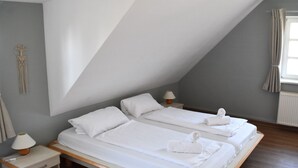 Un dormitorio con dos camas, una mesita de noche, una lámpara y una decoración de macramé en la pared.