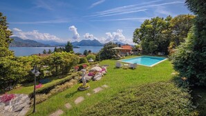 Una piscina con vista sulle montagne e un lago, circondata da un giardino curato e una casa.