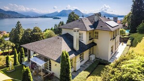 Una casa a due piani con un balcone, una piscina e vista su un lago e montagne.
