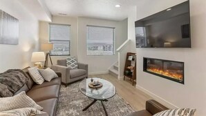 A modern living room with a sofa, armchair, and coffee table, a fireplace, and a TV mounted on the wall.