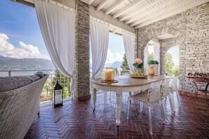 Una terraza con un muro de piedra, una mesa redonda con un florero y una silla de mimbre.