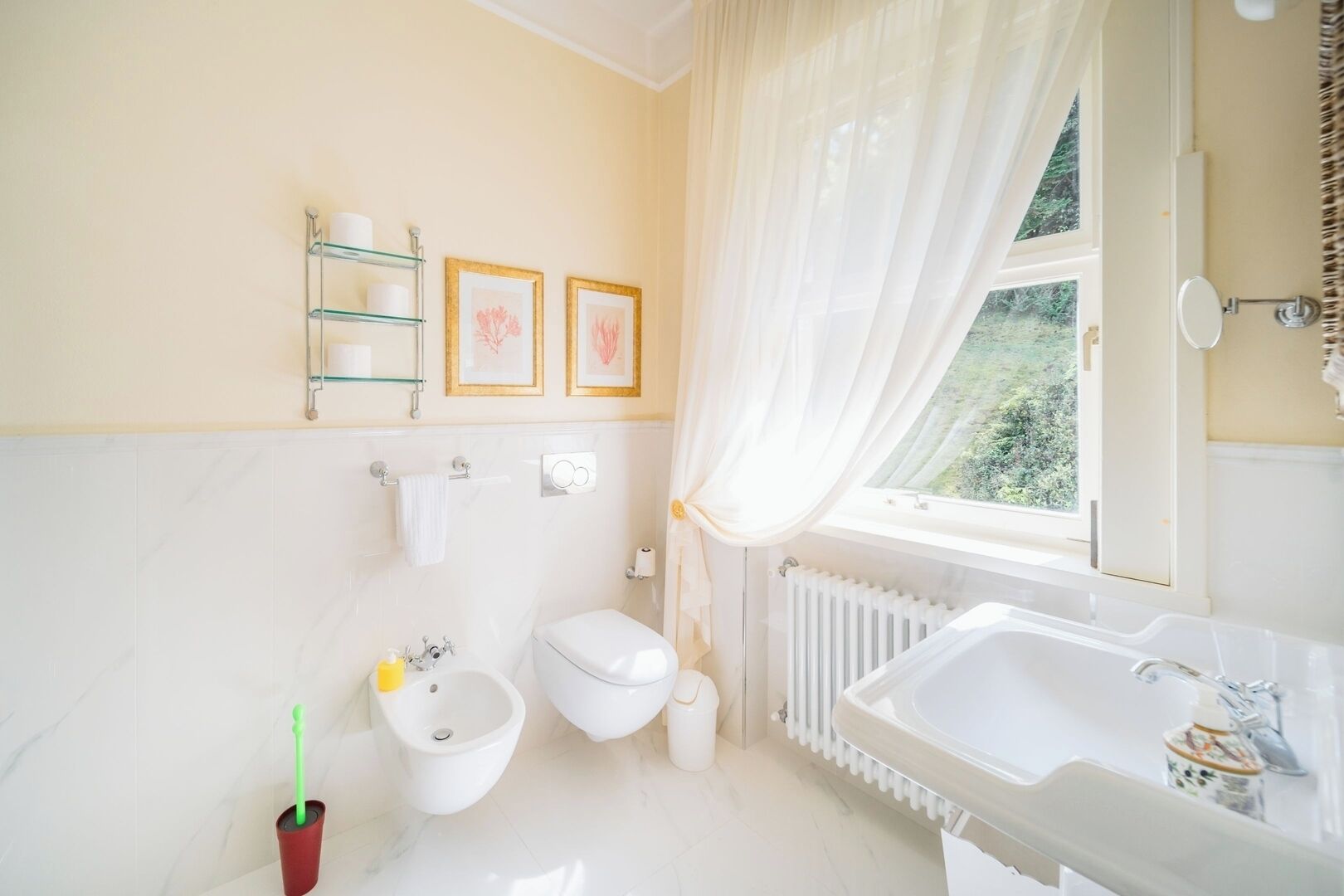 Une salle de bain équipée de toilettes, d’un bidet, d’un radiateur et d’une fenêtre avec des rideaux.
