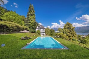 Une piscine avec des chaises longues, une maison et un paysage montagneux.