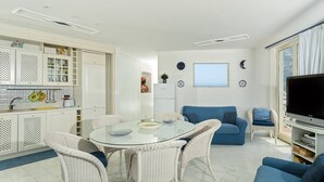 A modern living room with a glass dining table, white wicker chairs, a blue sofa, and a flat-screen TV. - Stella Di Mare, with pool and sea views (Positano)