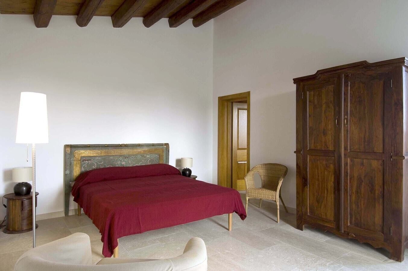 Un dormitorio con cama, armario, silla y lámpara.