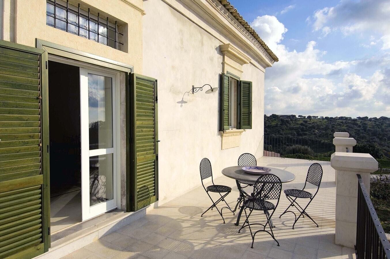 A terrace with a table and chairs, a sliding glass door, and a view of the countryside.