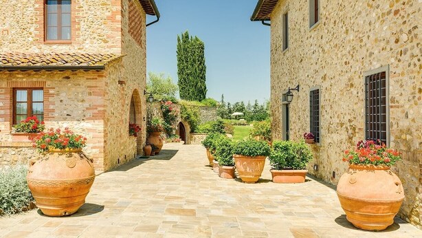 A stone pathway leading to a rustic building with terracotta pots and potted plants.