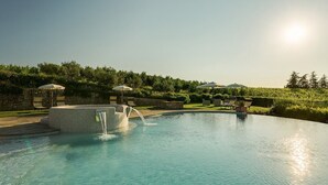 A clear swimming pool with a waterfall feature, surrounded by outdoor seating and a stone wall.