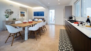 Une cuisine moderne avec un coin repas, comprenant une table en bois, des chaises blanches et un comptoir de cuisine équipé d’appareils électroménagers et d’une bouteille de vin.