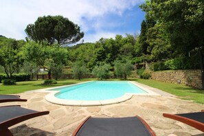 Piscina com ladrilhos de pedra e duas cadeiras de descanso.