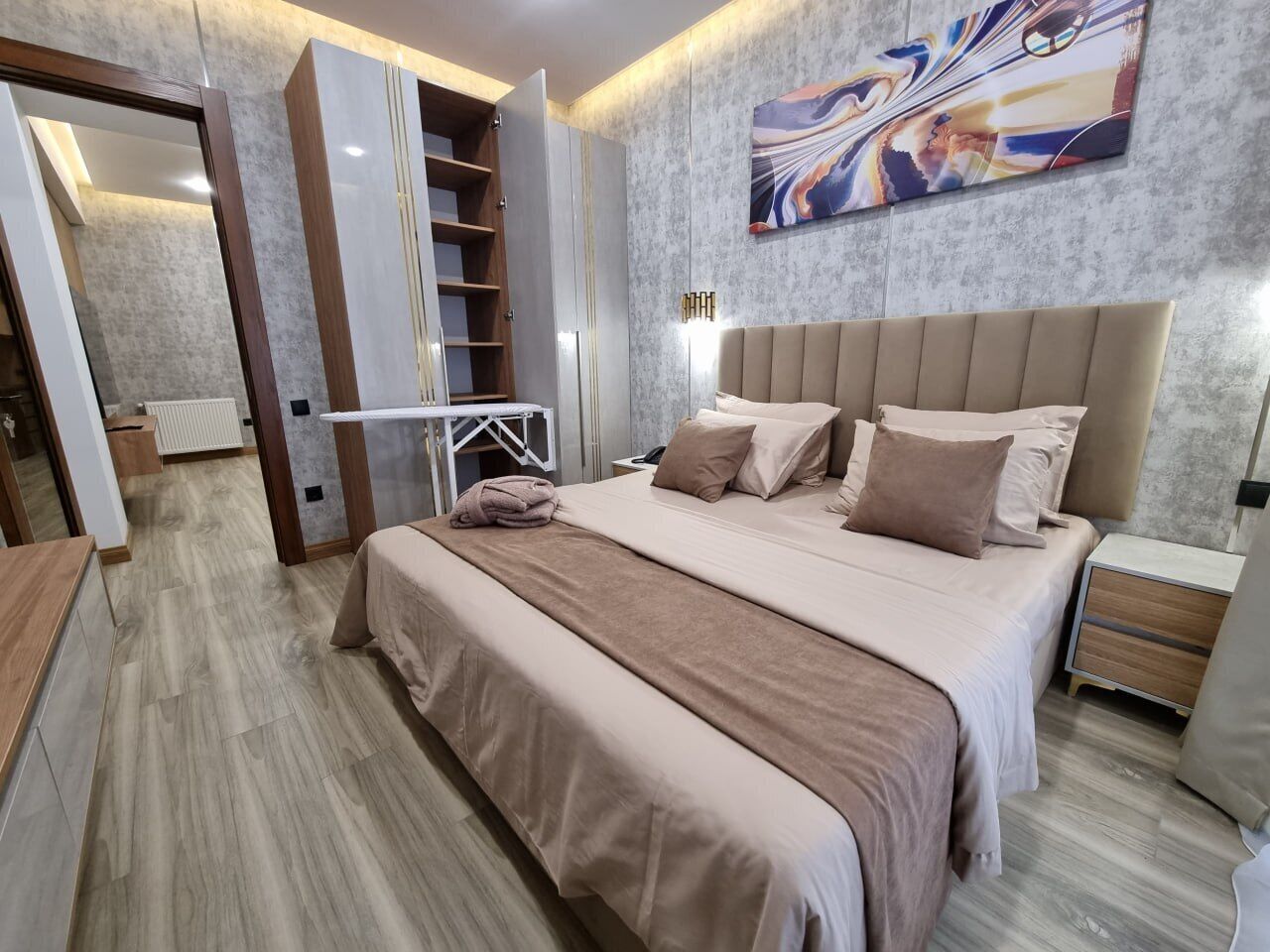 A modern bedroom with a large bed, a wardrobe, and a painting on the wall.