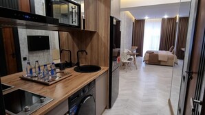 A modern kitchen with a dishwasher, sink, and wooden countertop. There is a dining area with a table and chairs, and a bedroom with a bed and curtains. - Badem Garden Apart Hotel (Tashkent)