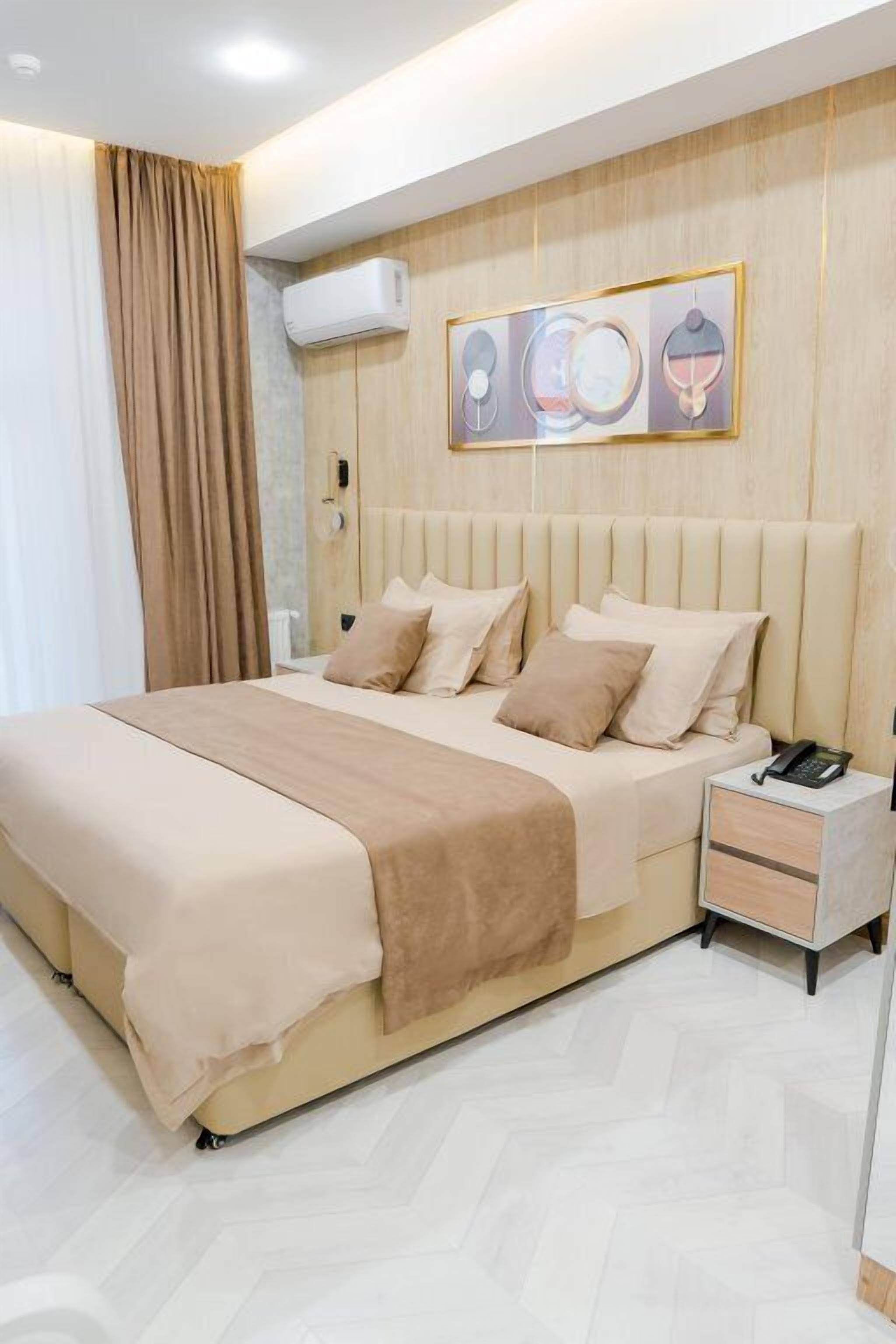 A modern hotel room with a large bed, a bedside table with a phone, and a wall-mounted air conditioner.