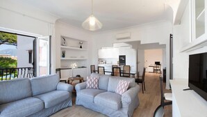 Un apartamento moderno con sala de estar que incluye dos sofás grises, una mesa de comedor con sillas, una zona de cocina y un televisor sobre un mueble.
