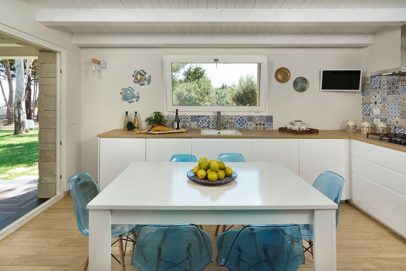 Une cuisine moderne avec des meubles blancs, un plan de travail en bois et un coin repas comprenant une table blanche et des chaises bleues.