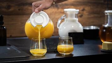 A hand pouring orange juice from a pitcher into two glasses on a countertop.
