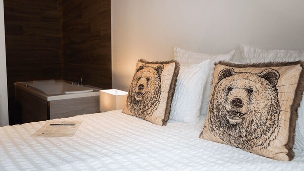 A hotel room with a bed, two pillows with bear designs, a bedside table, and a nightstand with a lamp. - Luxury residence in Métabief, suites, apartments, private spa and sauna (Métabief)