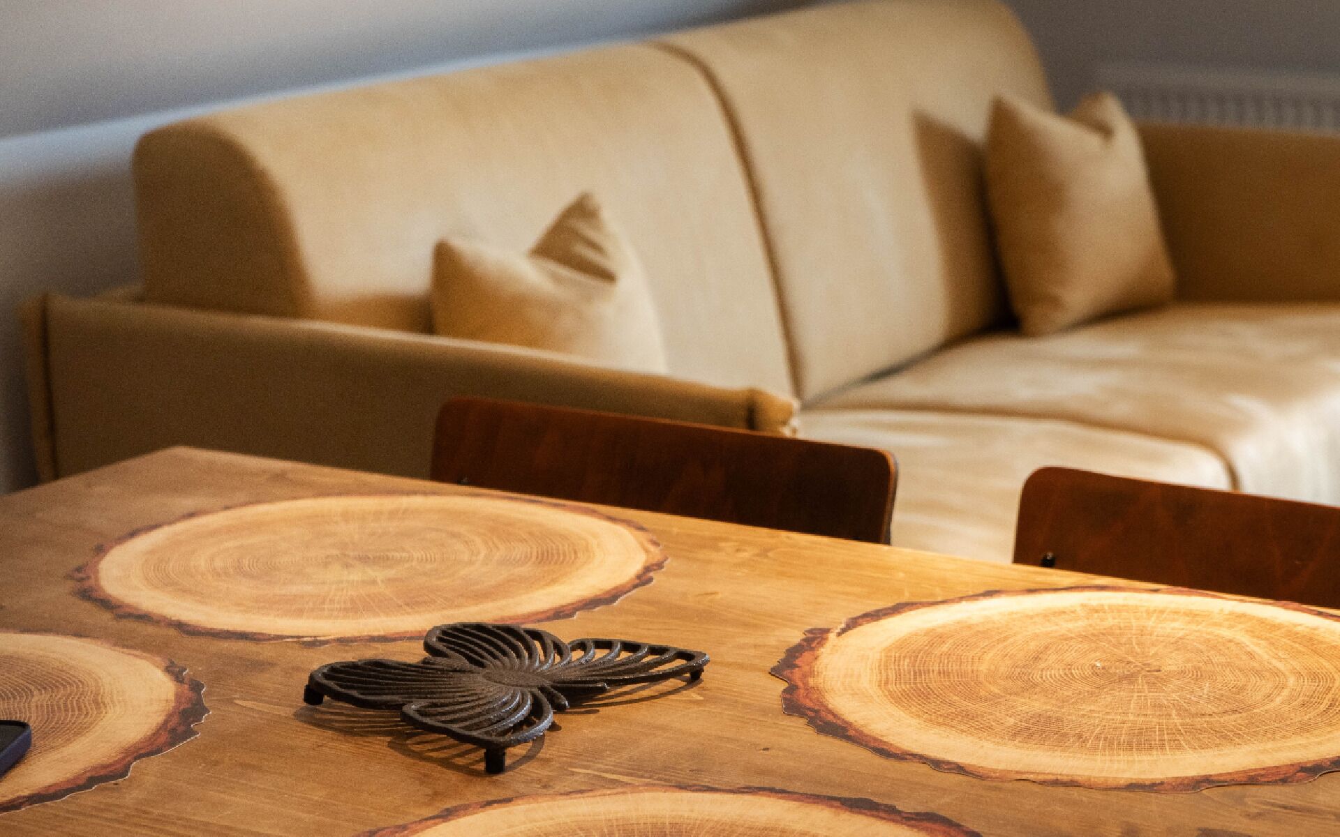 Una mesa de comedor de madera con un diseño único, un sofá color beige con cojines y sillas de madera en un ambiente de sala de estar.