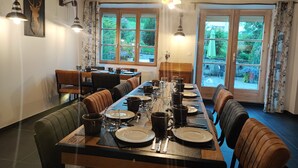 A dining area with a long table set for a meal, surrounded by chairs, with windows offering a view of the outdoors. - Luxury residence in Métabief, suites, apartments, private spa and sauna (Métabief)