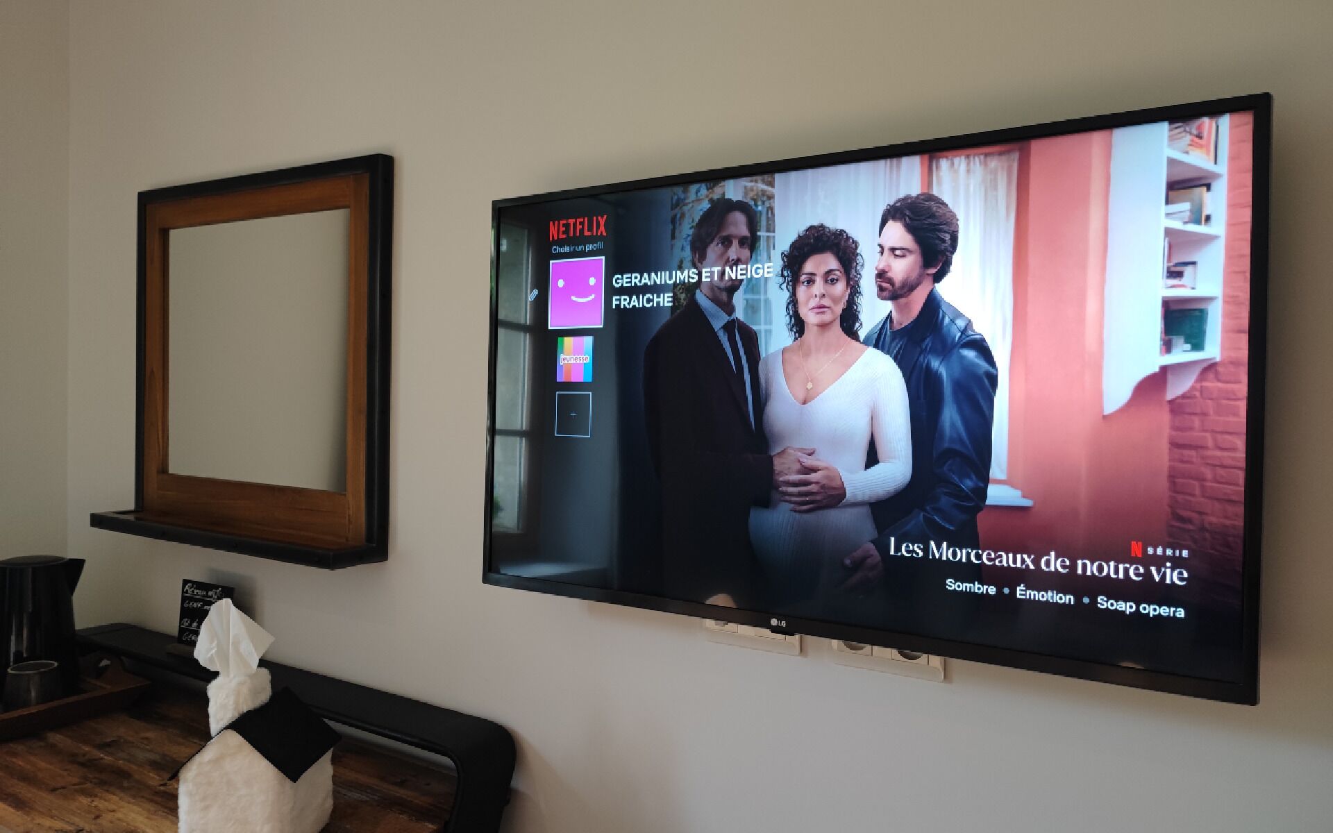 Un televisor montado en la pared mostrando una serie de Netflix titulada 'Les Morceaux de notre vie' con subtítulos.