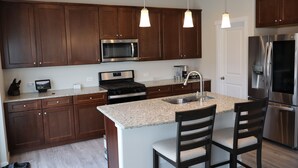A modern kitchen with dark wooden cabinets, stainless steel appliances, granite countertops, and pendant lighting. - Spacious 5-BR Home: Private Hot Tub & Big Yard, Stocked Kitchen, Mountain View! (Colorado Springs)