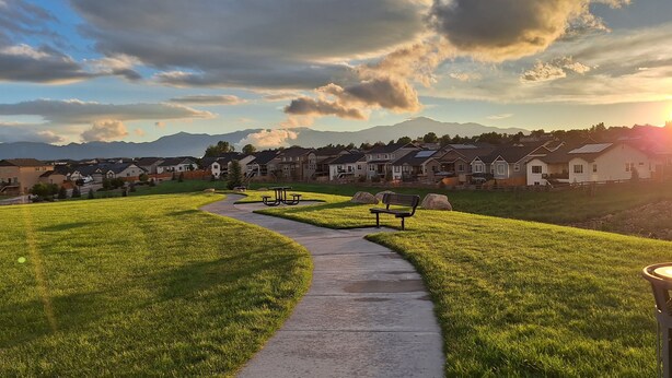 A residential area with houses, a winding path, benches, and a clear view of mountains in the background. - Spacious 5-BR Home: Private Hot Tub & Big Yard, Stocked Kitchen, Mountain View! (Colorado Springs)