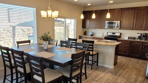 A modern kitchen with dark wooden cabinets, a central island, and a dining area with a table and chairs. - Spacious 5-BR Home: Private Hot Tub & Big Yard, Stocked Kitchen, Mountain View! (Colorado Springs)