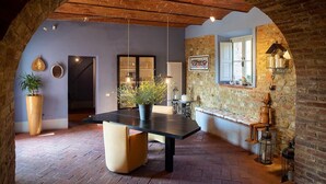 Comedor con una mesa negra, sillas color beige, una planta en maceta y una pared de piedra con una ventana.