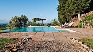Piscina privada con una pérgola, sillas de descanso y vistas al campo.
