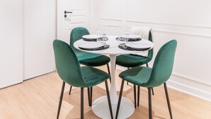 A dining area with a round table, four green chairs, and a pendant light.