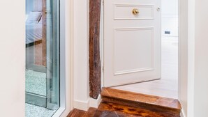 A hallway with a wooden floor, a glass door, and a white door with a brass handle.