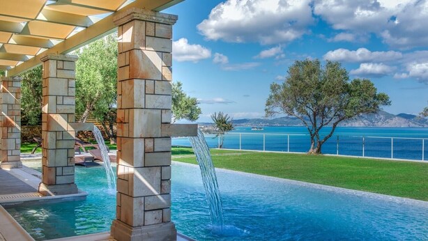 A pool area with a stone structure, a waterfall feature, and a view of the sea and mountains. - Villa Zenais, Luxury with swimming pool (Koridallos)